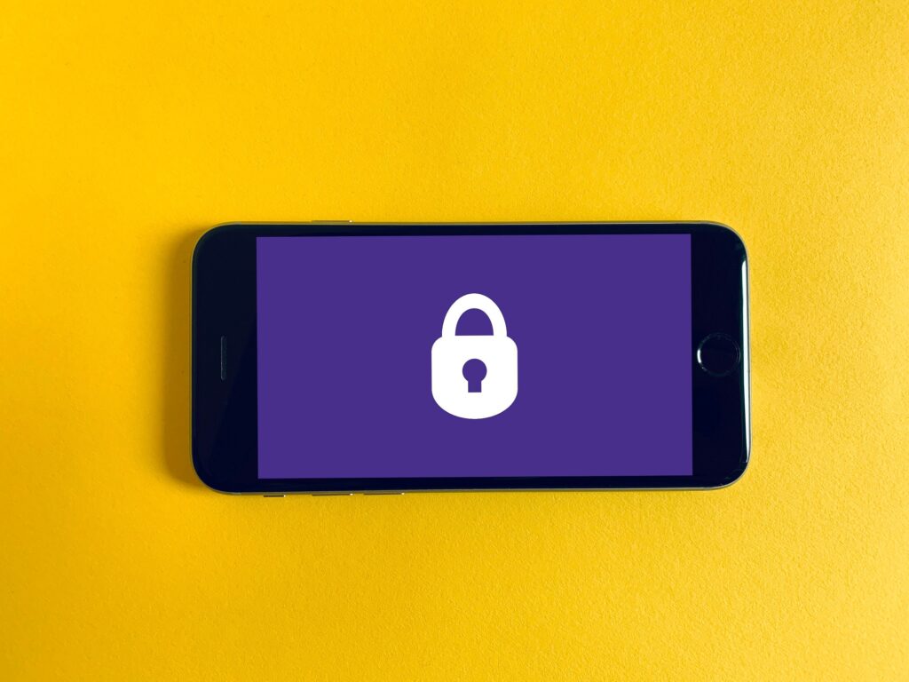 Photo of a smartphone centered on a yellow surface. The phone screen shows a white padlock icon on a purple background.