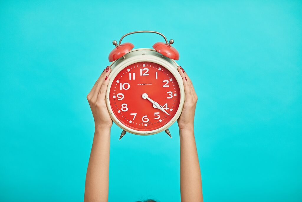 photo of two hands holding up an analog alarm clock against a blue background
